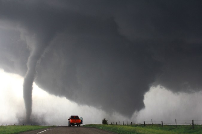 Red pickup truck stopped in front of a tornado in Nebraska