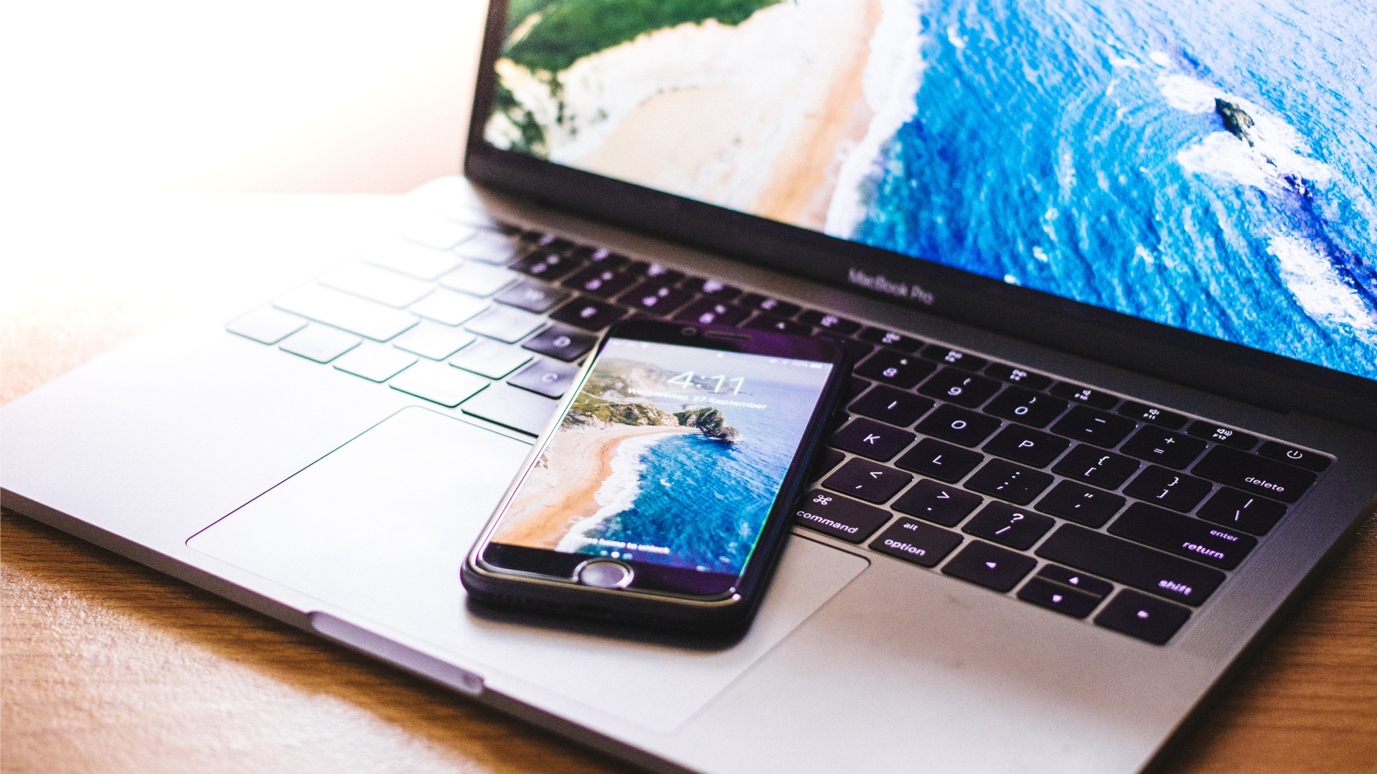 An iPhone on top of the keyboard of a Macbook laptop, getting ready to back up photos to the cloud.