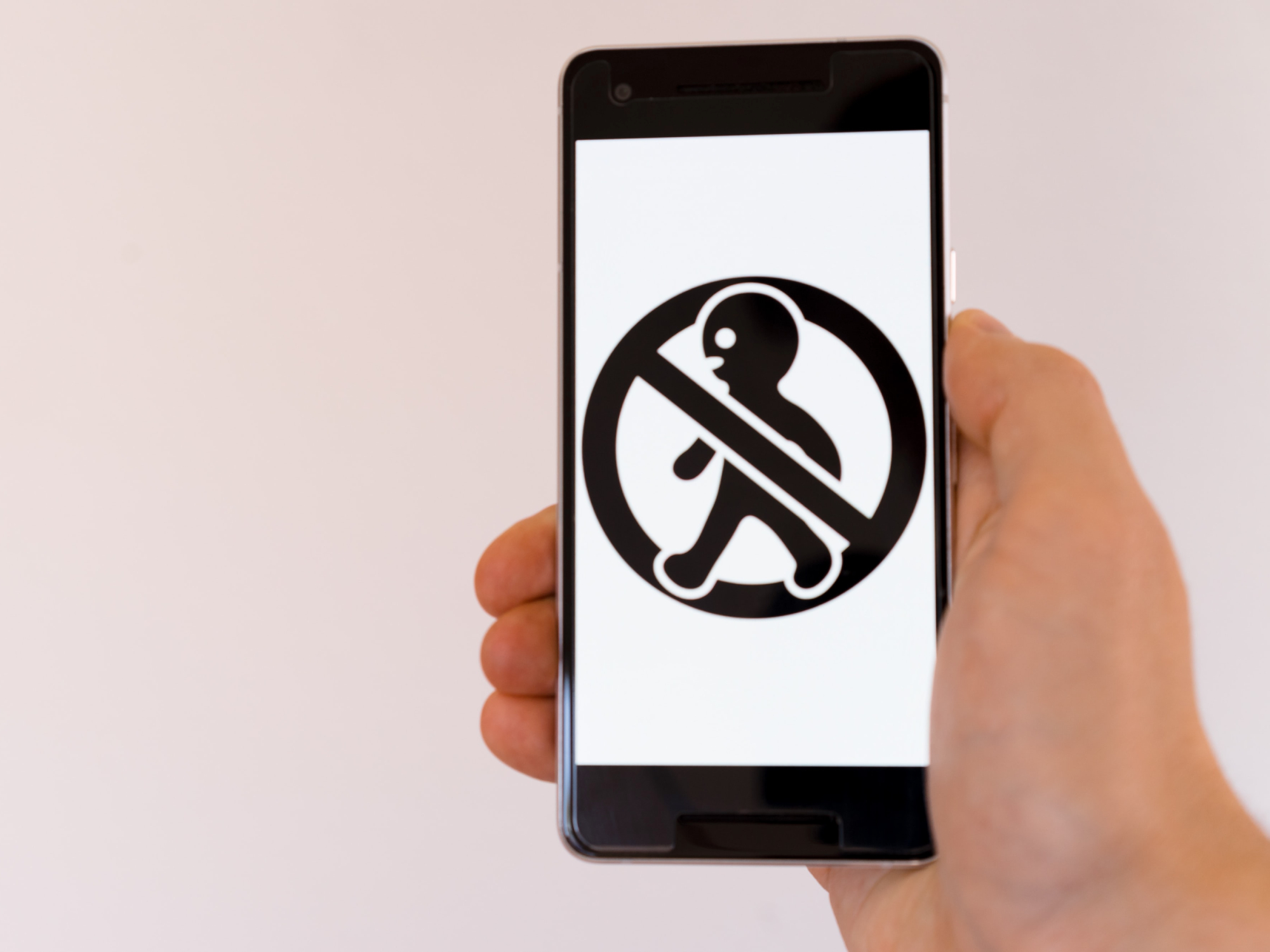 A person holding a smartphone with a crossed-out image of a person's silhouette on it.