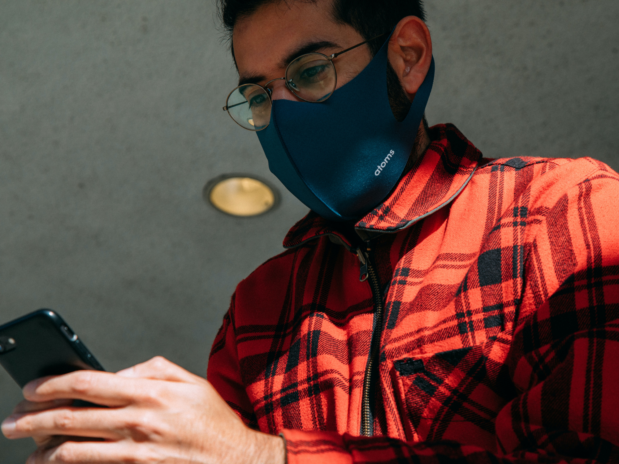 A person using their phone while wearing a face mask and wearing a red plaid shirt.