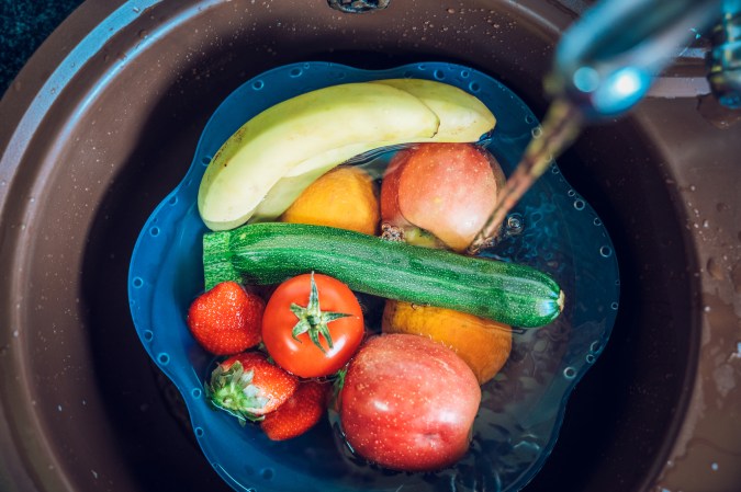 Blue basin full of fruits and vegetables with tap water in the kitchen sink. Disinfecting fruits and vegetables to prevent the spread of the coronavirus.