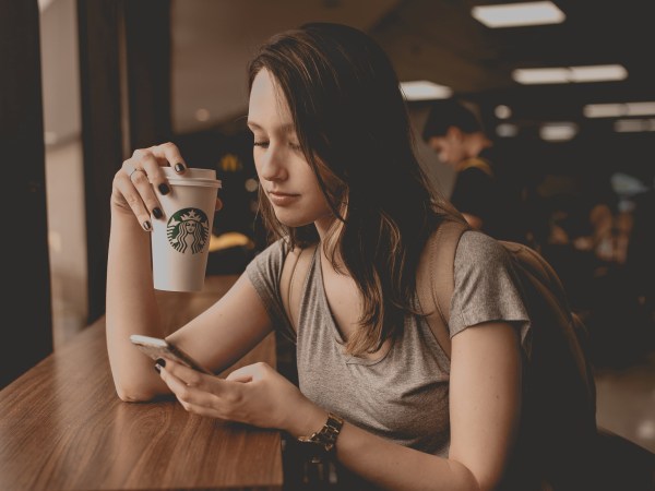 A woman looking at her phone while sitting at the window bar inside a Starbucks.