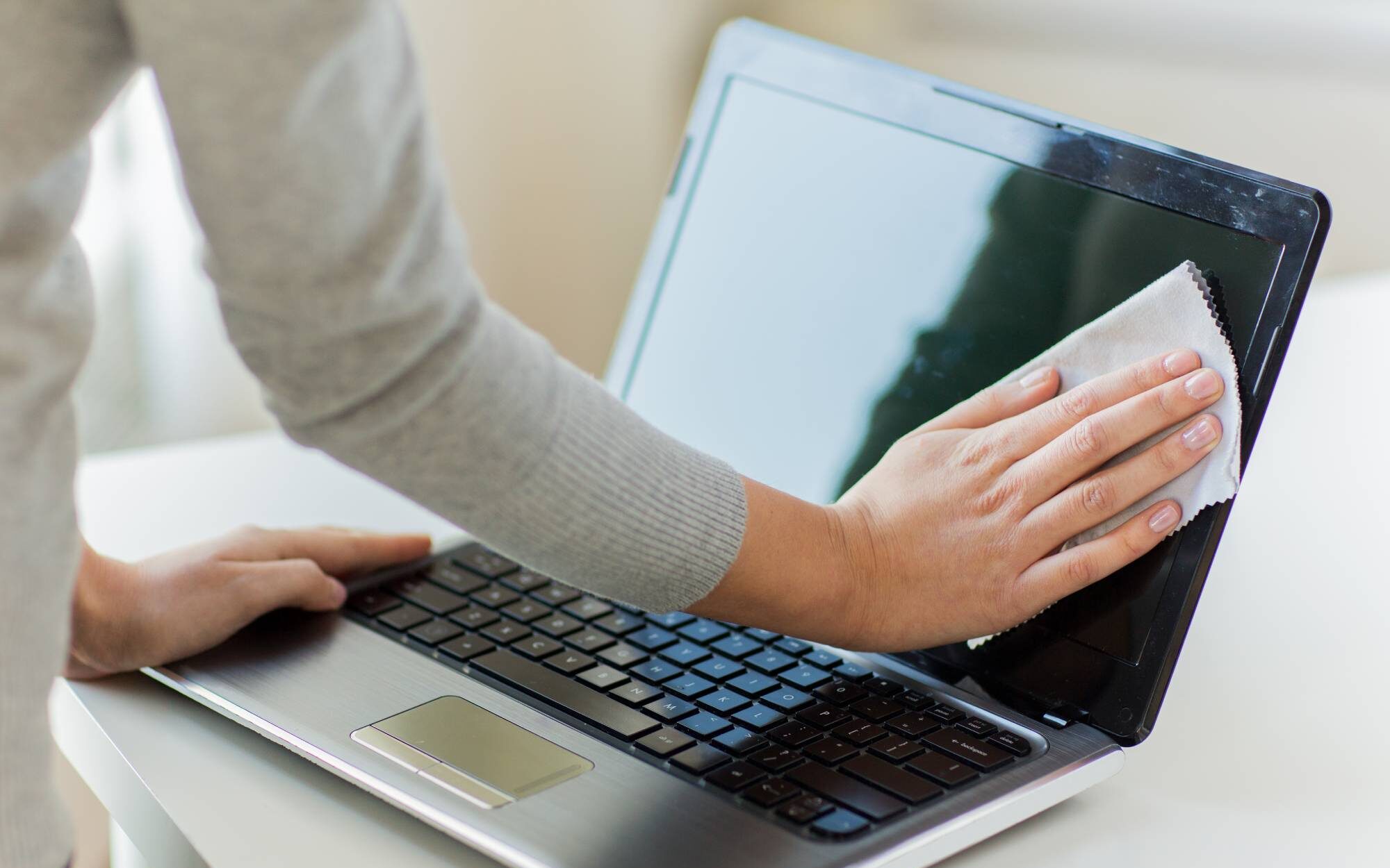 Person cleaning the screen of a laptop with a cloth as part of their digital spring cleaning.