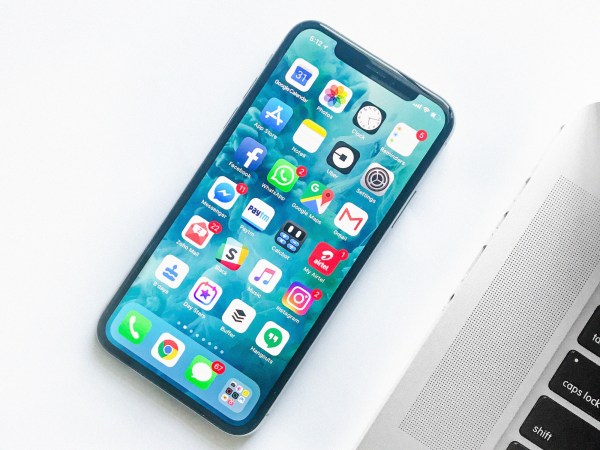 An unlocked iPhone on a white table with its apps showing various notification icons and alerts.