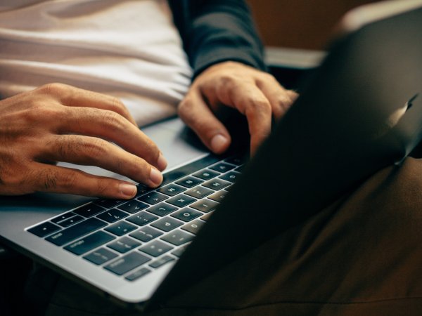 A person sitting with a black laptop on their lap, with their hands on the keyboard, ready to type.