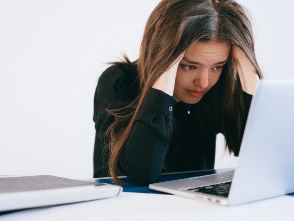 A woman wearing a black shirt leaning over a dead computer with her hands on her temples, wondering how she can get her silver Macbook to turn back on, or how she can recover files from it.