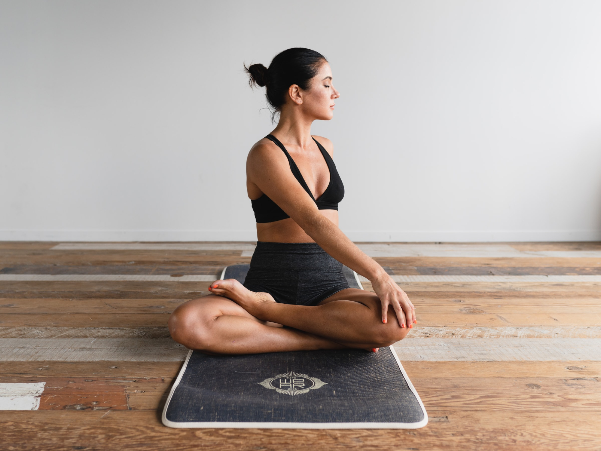 A woman sitting cross-legged on a yoga mat, rotating her torso to stretch her back.