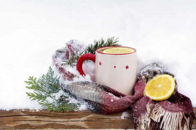 a mug with lemons and tea sitting on a snow-covered table 