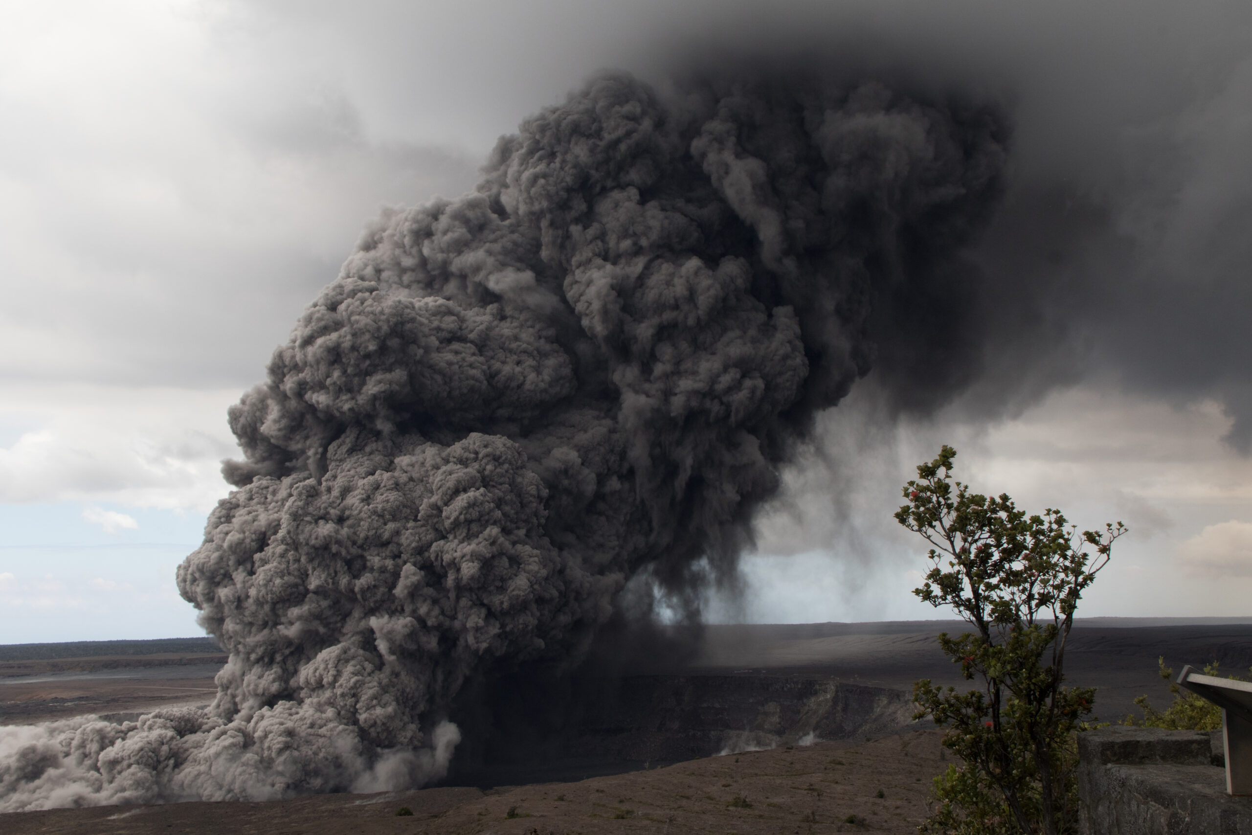 cloud of dark smoke rising out of the ground towards white clouds