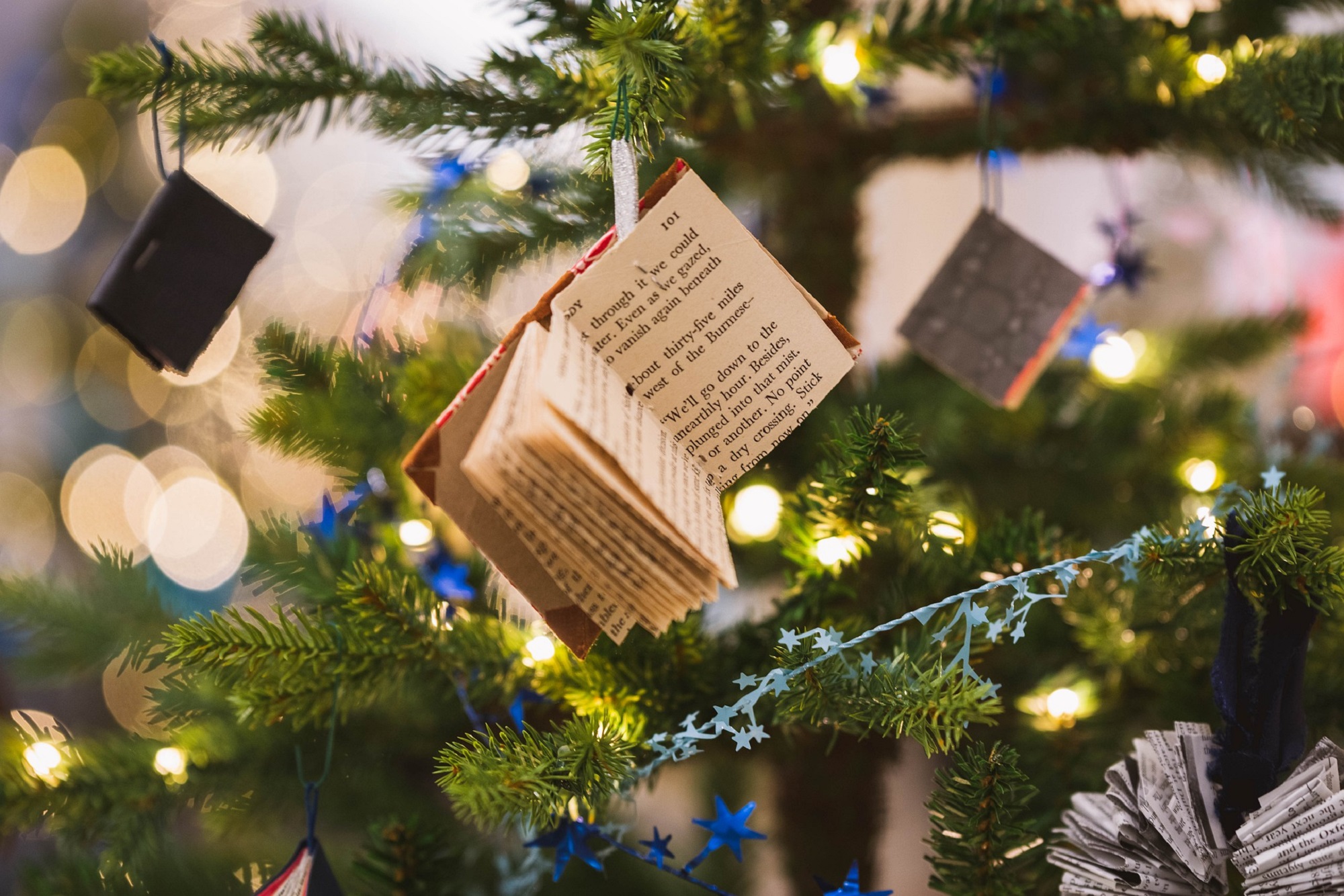 Fresh Christmas tree with white lights, star tinsel, and book ornaments