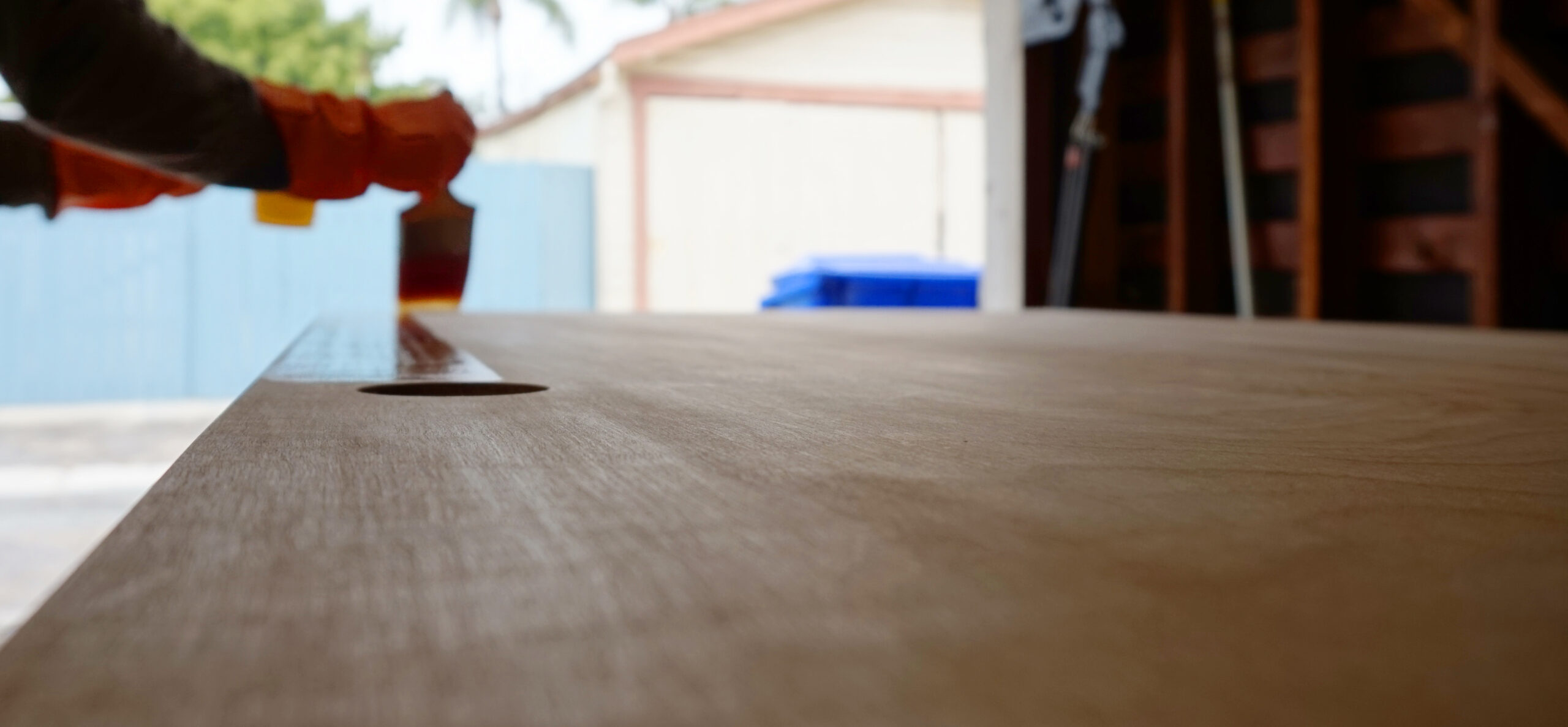 A person applying stain to the surface of a wooden door that will serve as the top of a DIY computer desk.