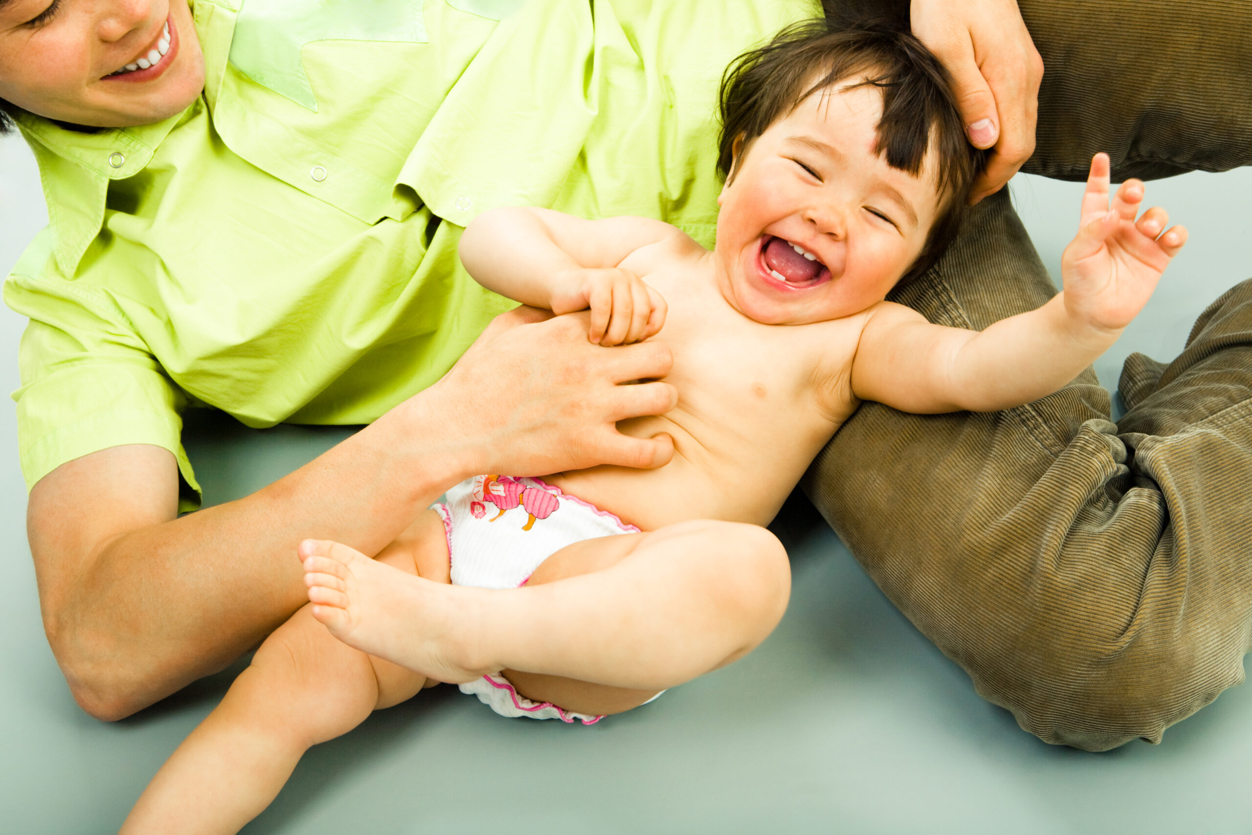 a woman tickles a smiling baby 