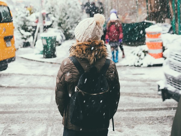 A person standing by the side of a street while snow falls in the winter.