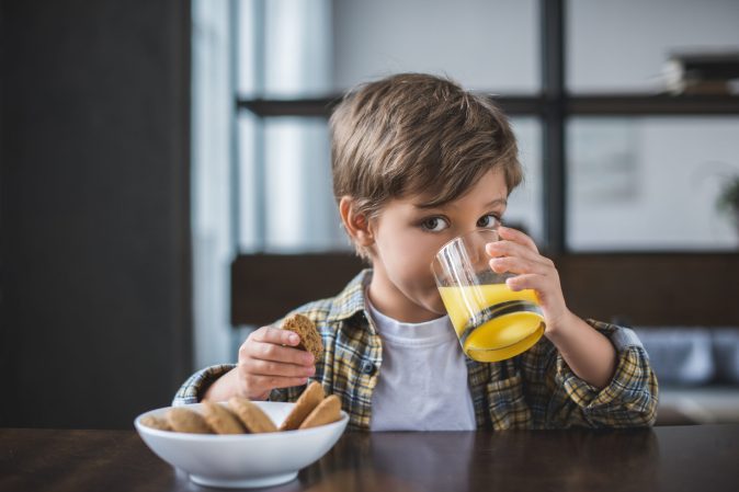 a young boy drinks juice and eats cookies