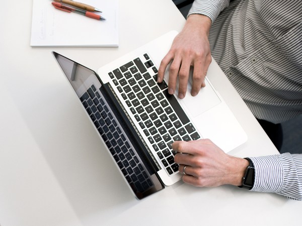 A person using a white MacBook laptop on a white table, maybe figuring out how to remove bloatware.