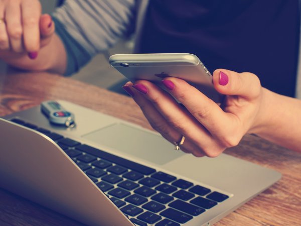 A person holding an iPhone while sitting in front of a laptop, possibly setting up a burner phone number.