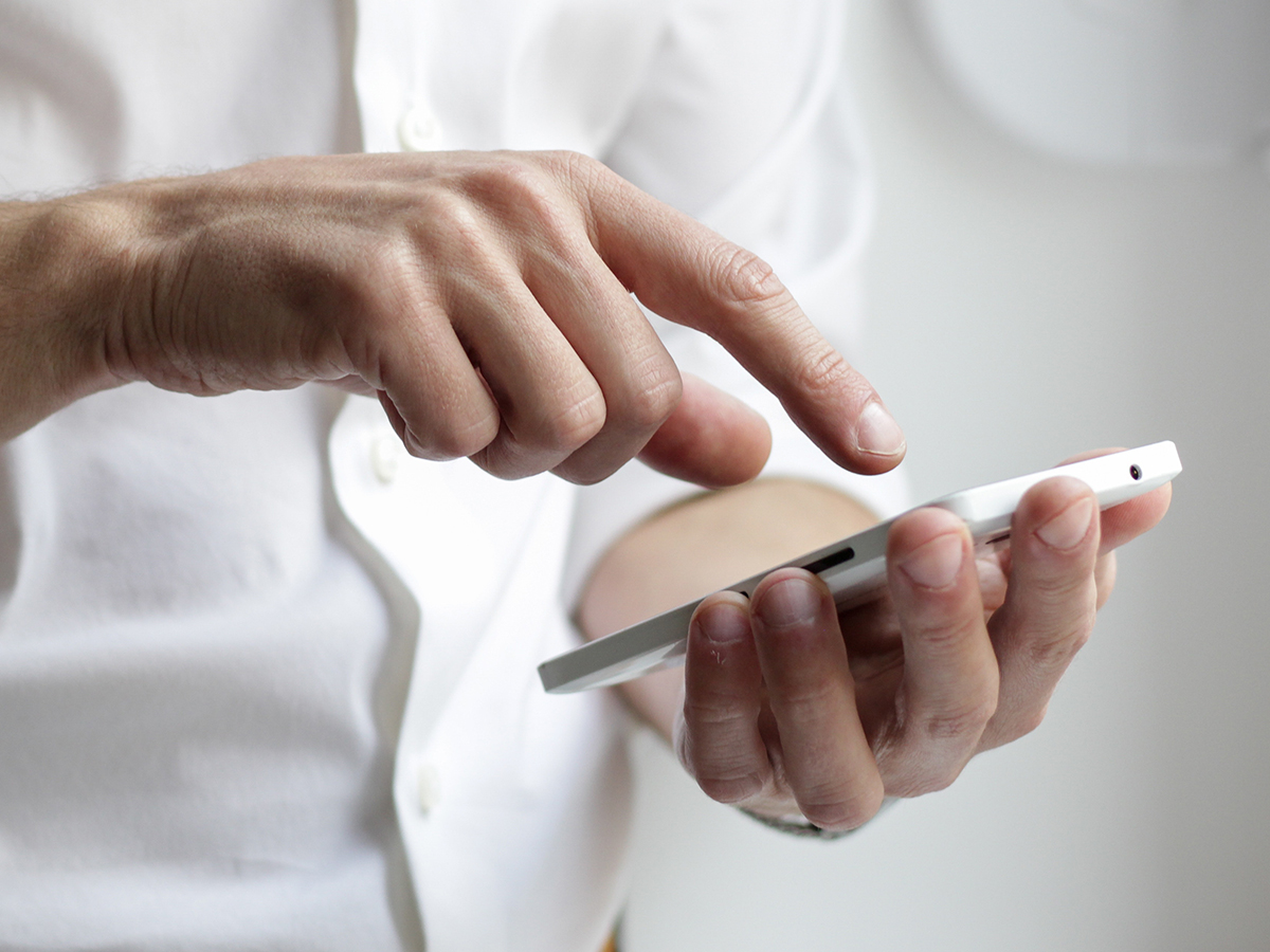 A person wearing a white buttondown shirt tapping on their smartphone.