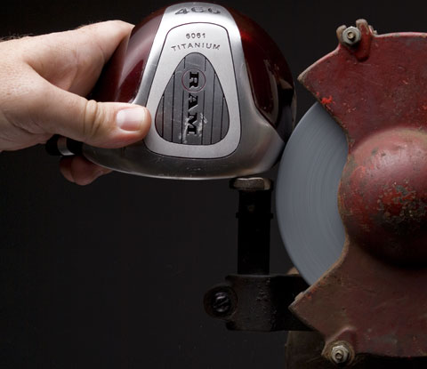 A person holding an aluminum golf club up to a grinder.