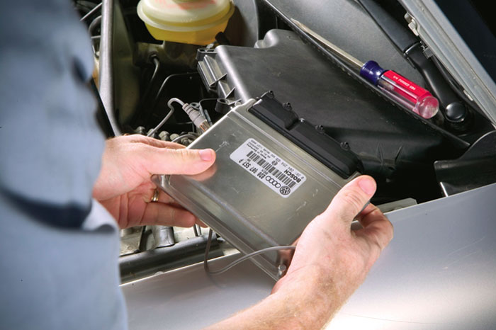 A person removing the engine control unit, or ECU, from under the hood of a silver car.