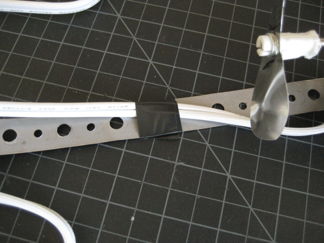 An electrical power cord taped to a metal bracket on top of black grid paper.
