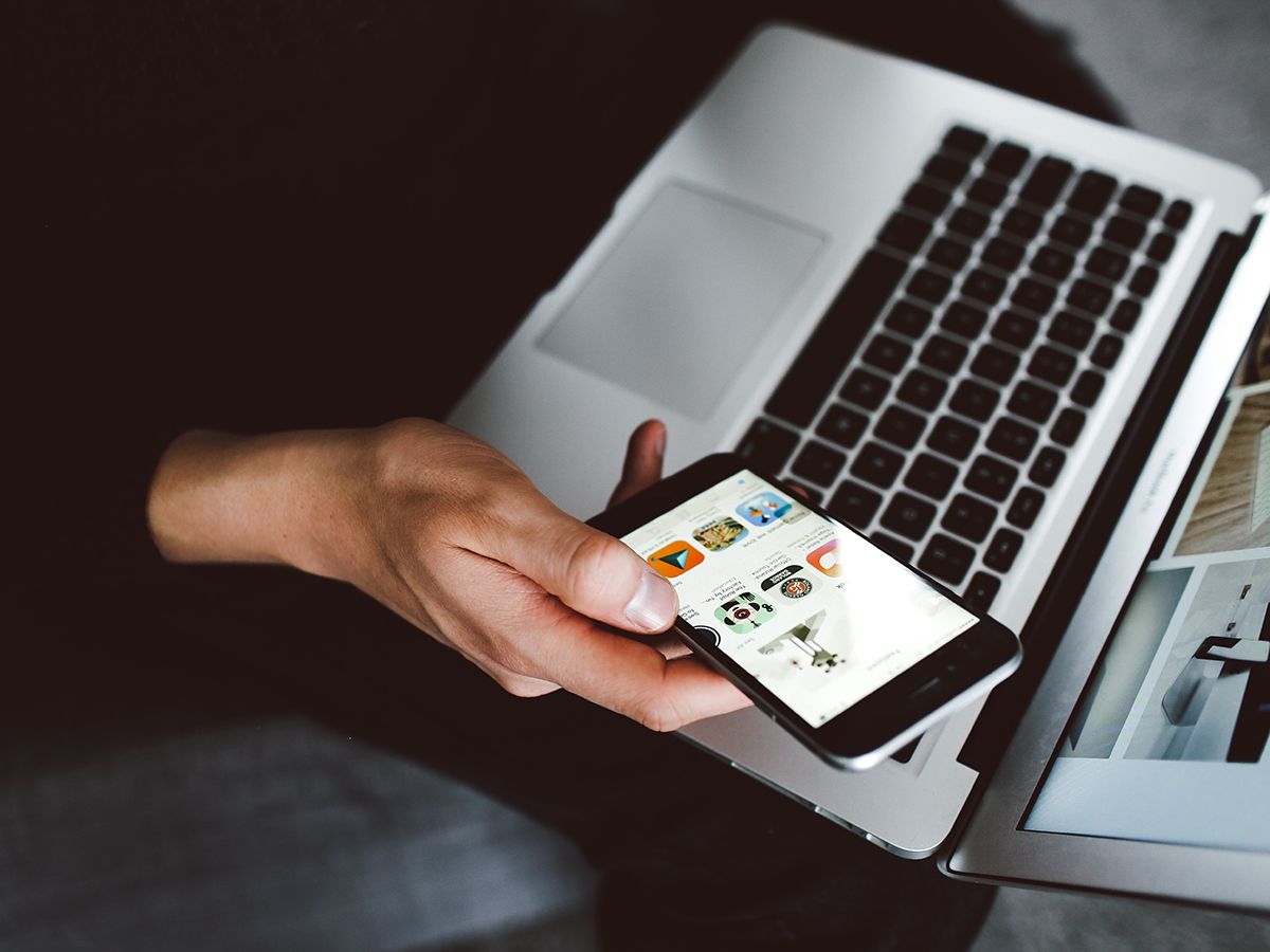 A person holding a phone over a laptop.