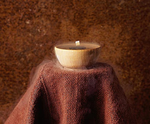 A white bowl on a small tablecloth-covered table against a brown background, with a small white object hovering above it.