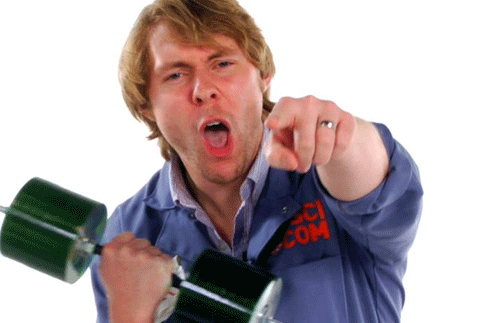 A man in blue Popular Science coveralls holding a dumbbell made out of old CDs, pointing at the camera, and yelling.