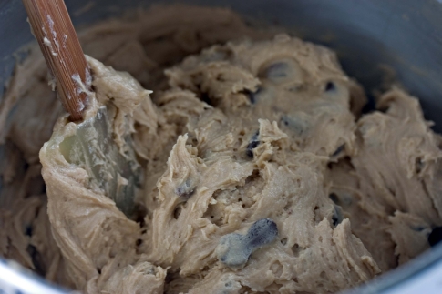 A wooden spoon mixing chocolate chip cookie dough in a bowl.