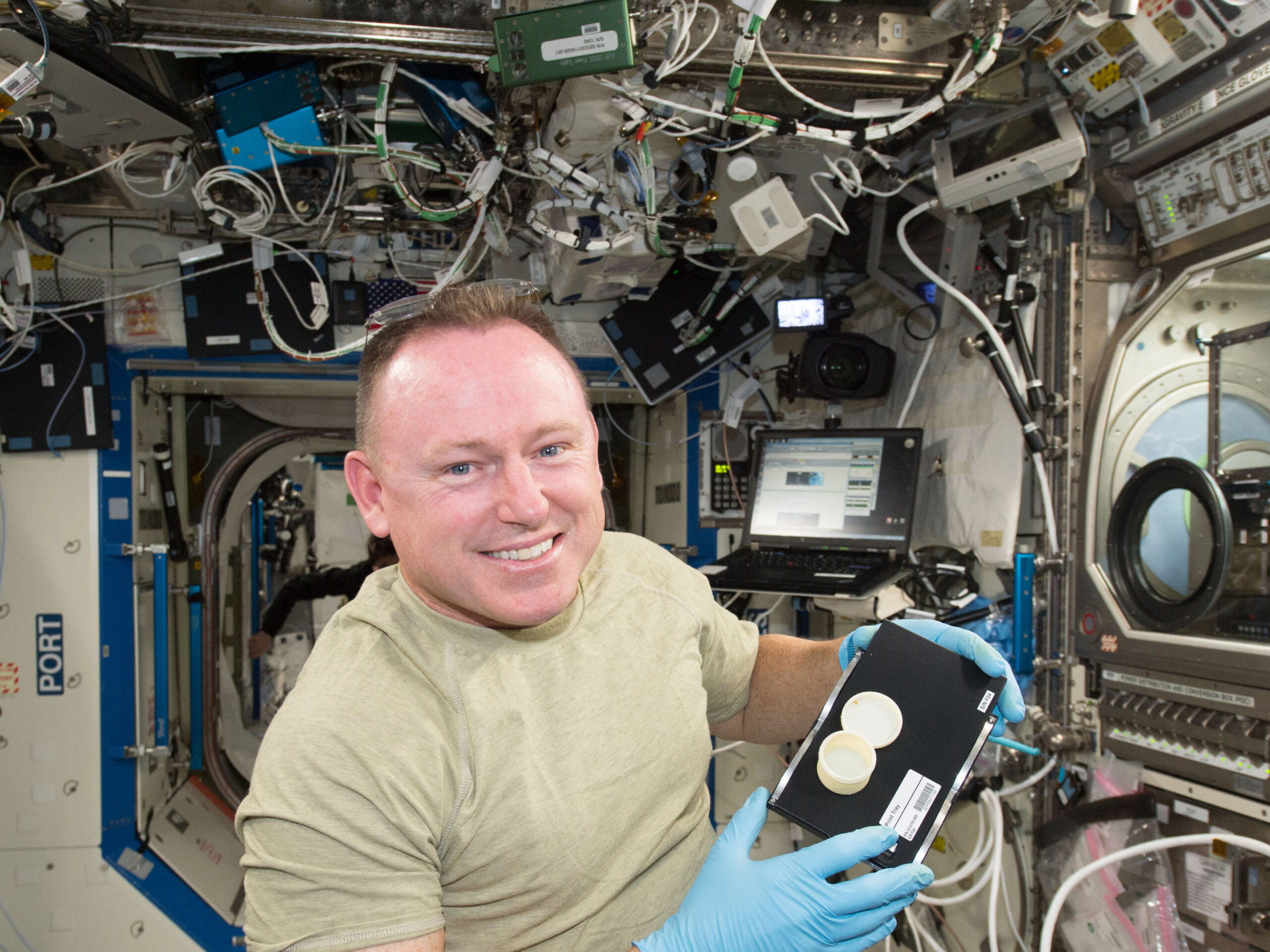 Astronaut Butch Wilmore holds a container that was 3D printed on the International Space Station.