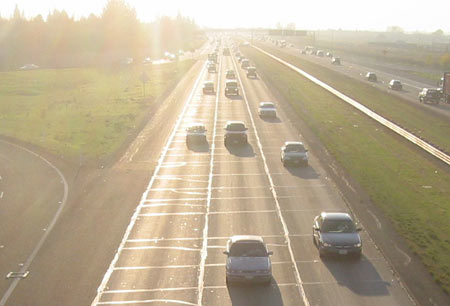 A Toyota Corolla driving down a freeway with a number of other cars, with the sun in the background.