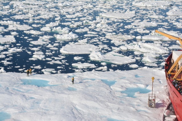 people standing on sea ice, ship to the right of them