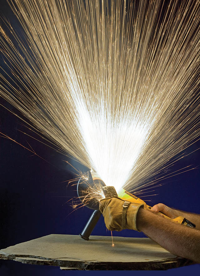 A person using a grinder to create a spray of white sparks from a piece of a bicycle.
