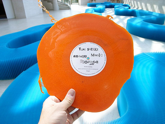A person holding an orange homemade vinyl record in front of some blue, horseshoe-shaped couches.