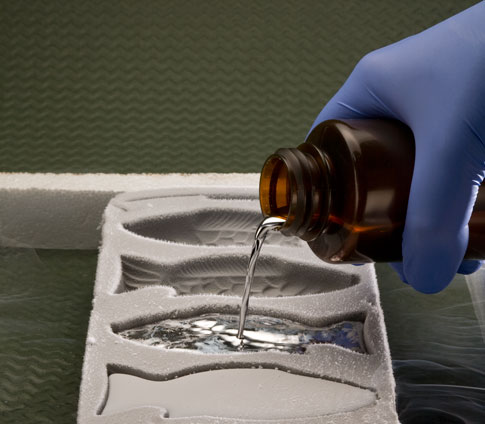 A person wearing blue rubber gloves pouring liquid mercury into a fish mold.