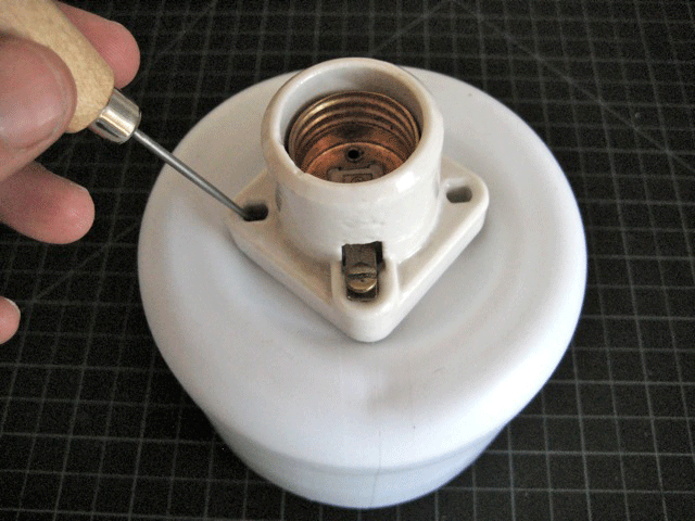 A person using a small screwdriver to attach a light bulb socket to the top of a cut-off bleach jug.