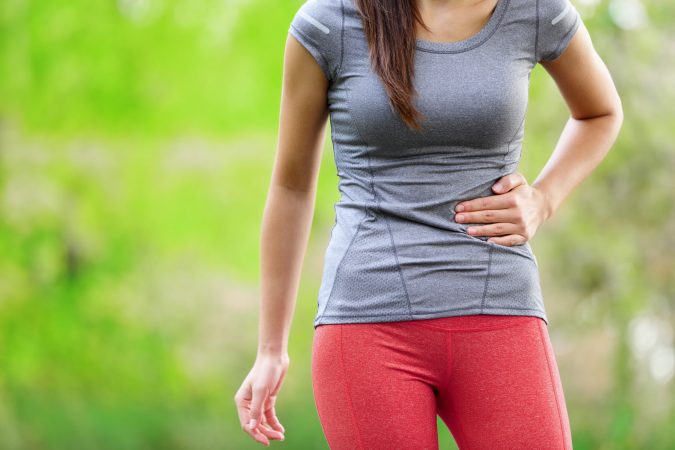 Person in gray exercise shirt and pink running tights with a side stitch