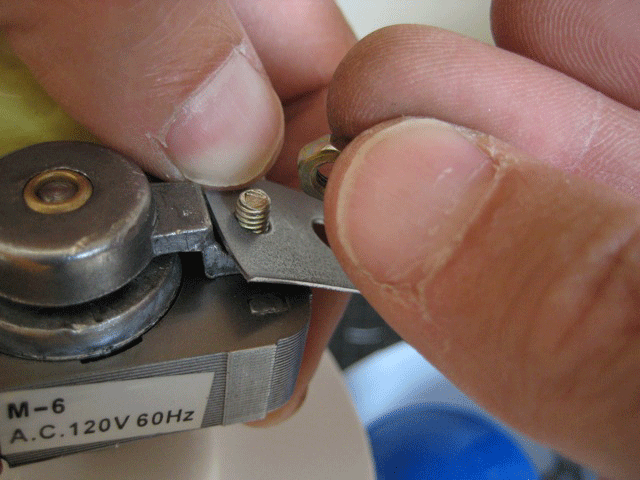 A person attaching a metal bracket to a small motor with screws.