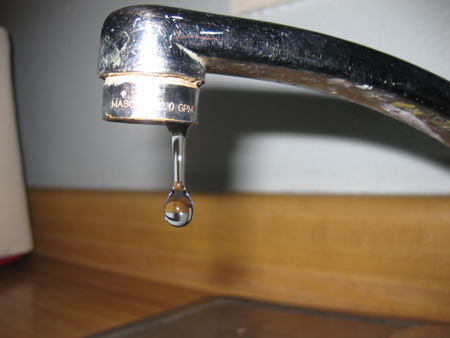 A silver sink faucet dripping water.