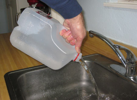 A person dumping a gallon jug of water into the sink.