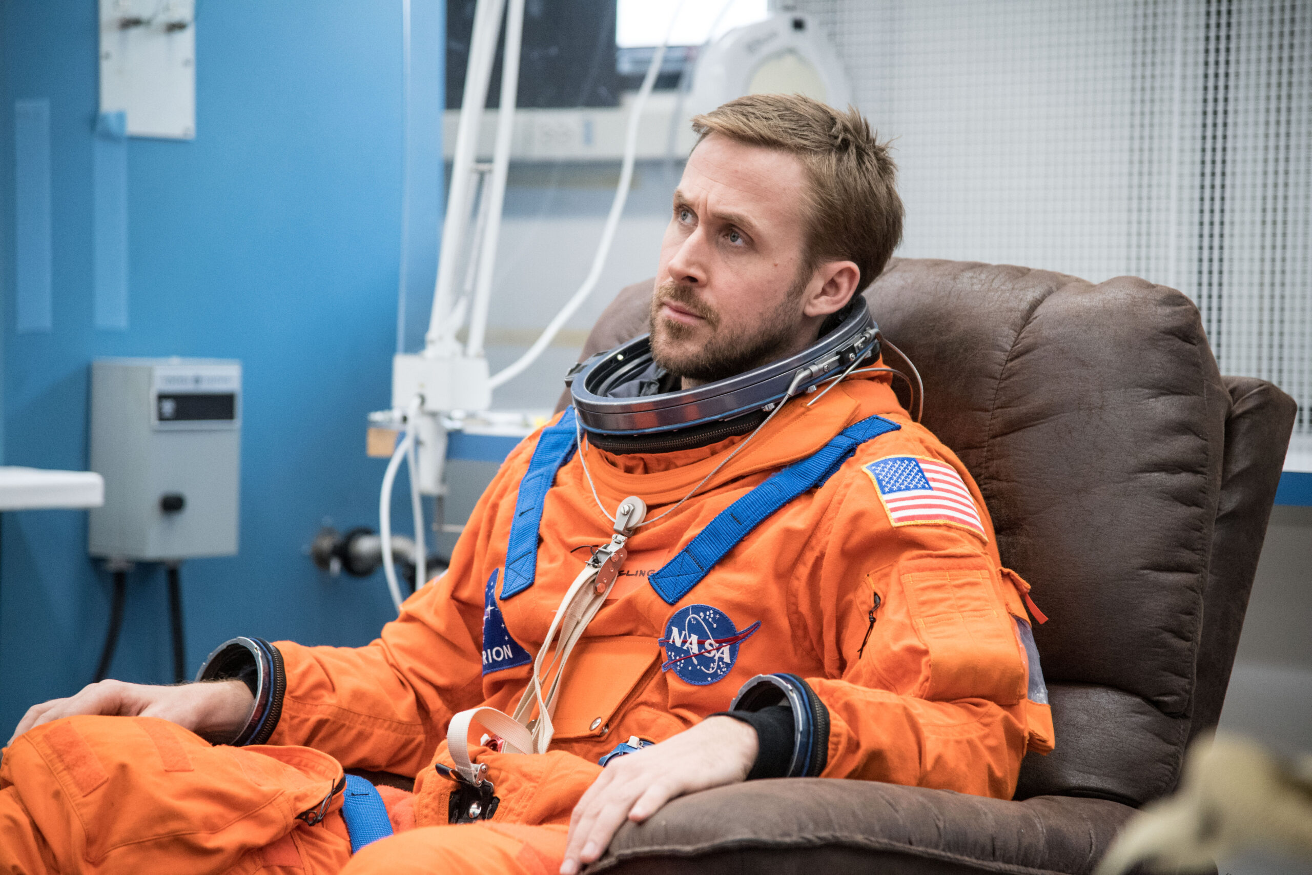 ryan gosling sitting in orange NASA uniform