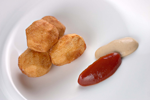 Four balls of fried, smoked potatoes stacked on a white plate next to some yuzu-kosho ketchup.