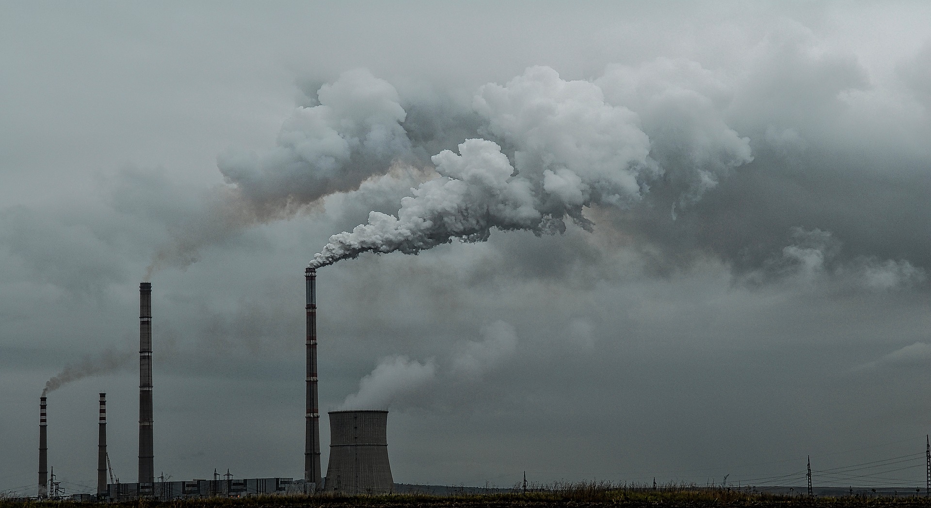 Smoke billows out of tall cement smokestacks against a grey sky.