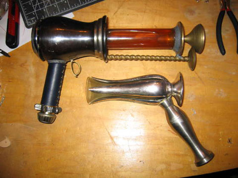 Two homemade steampunk ray guns, one smaller than the other, on a wooden surface.