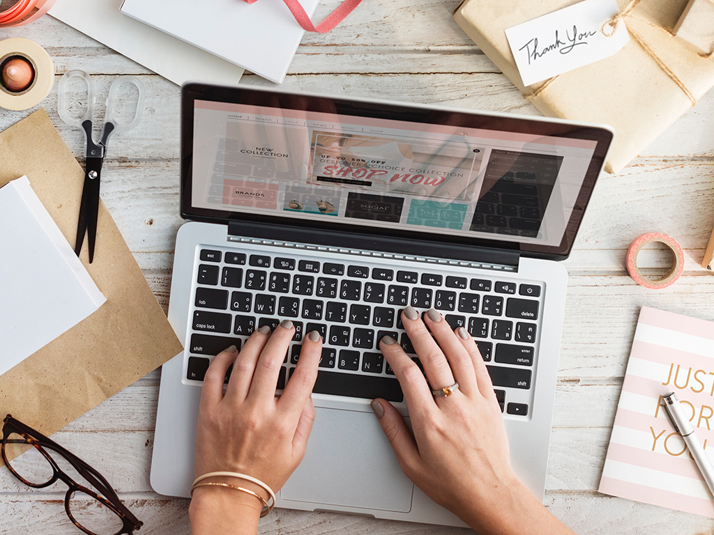 a person using an Apple laptop on a wooden desk with various materials around