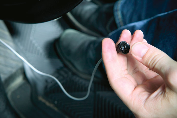 A person in the driver's seat of a car holding an external button for the vehicle's ECU.