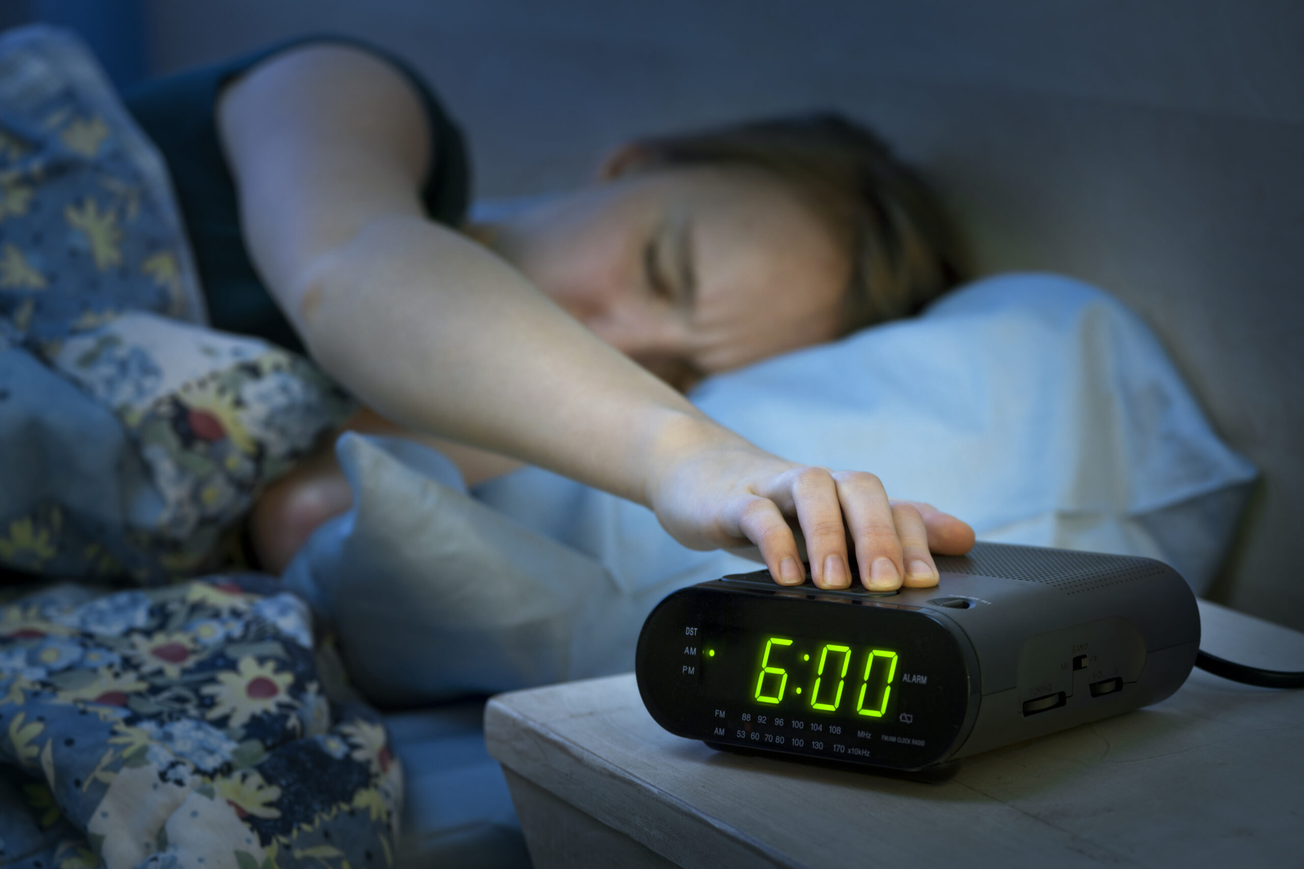 A woman snoozing an alarm clock at 6 a.m. in a dim room