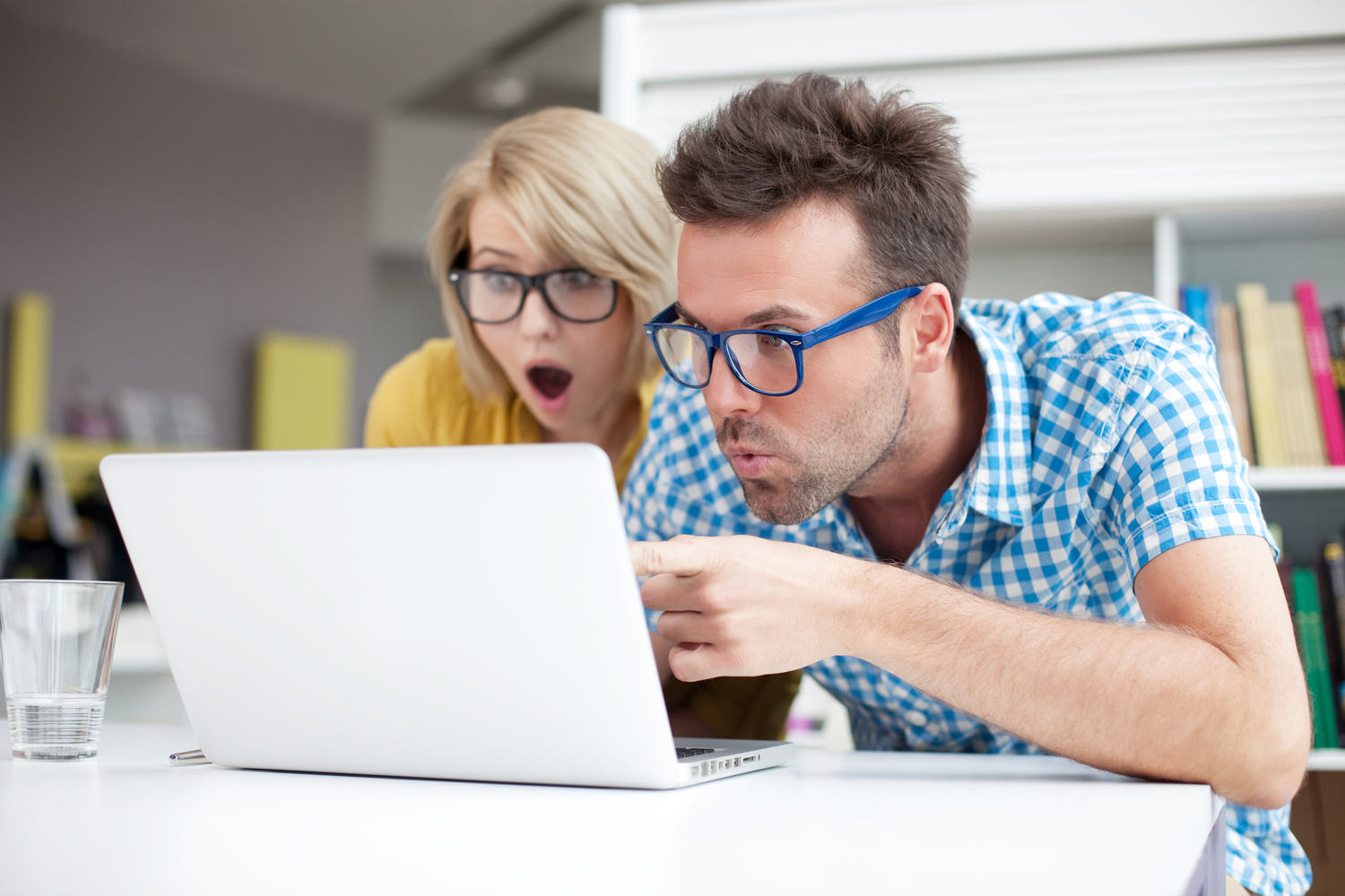 Two surprised students learning in a library on a laptop.