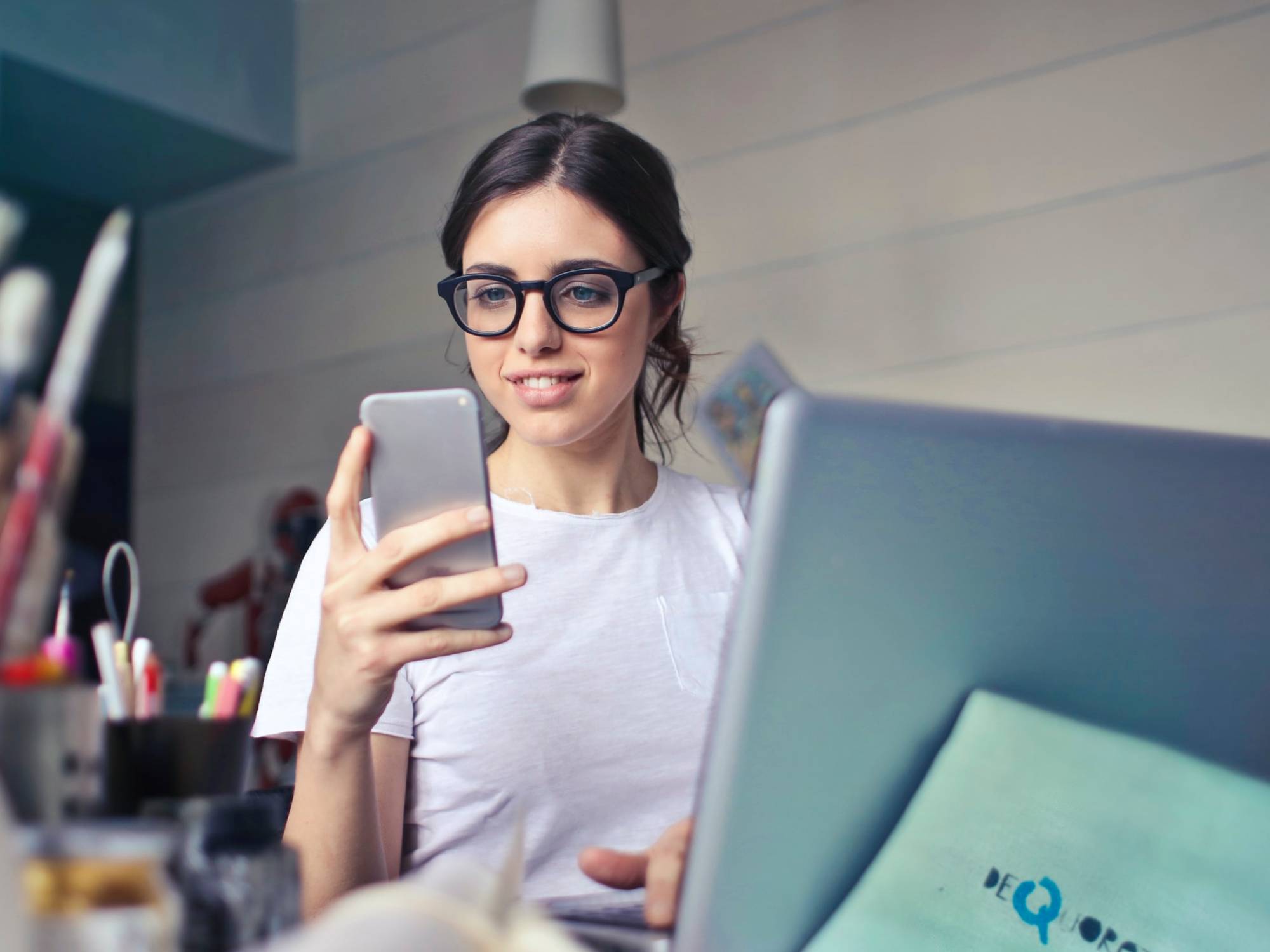 person-workilooking at phone and typing on laptop