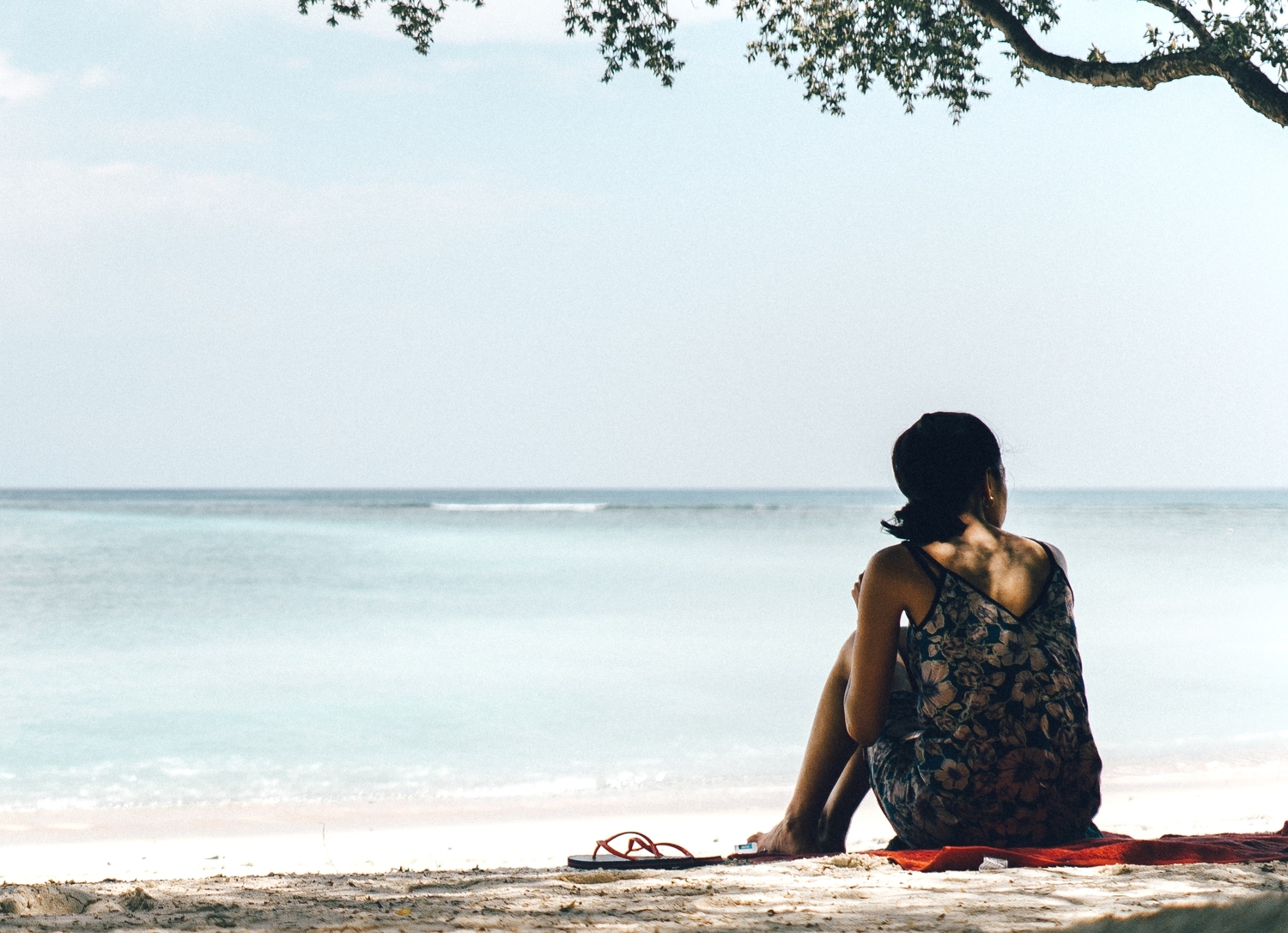 Woman sat on the beach under the shade of a tree