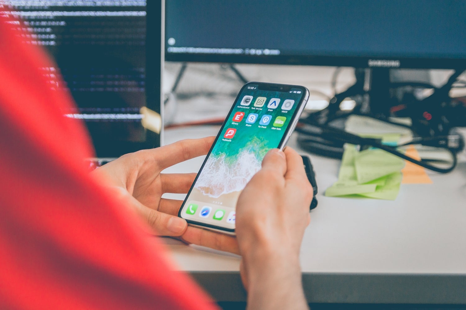 A person sitting at a desk and looking at their iPhone, perhaps trying to figure out how to customize it.